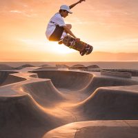 man in white t-shirt and brown pants riding skateboard on brown sand during daytime